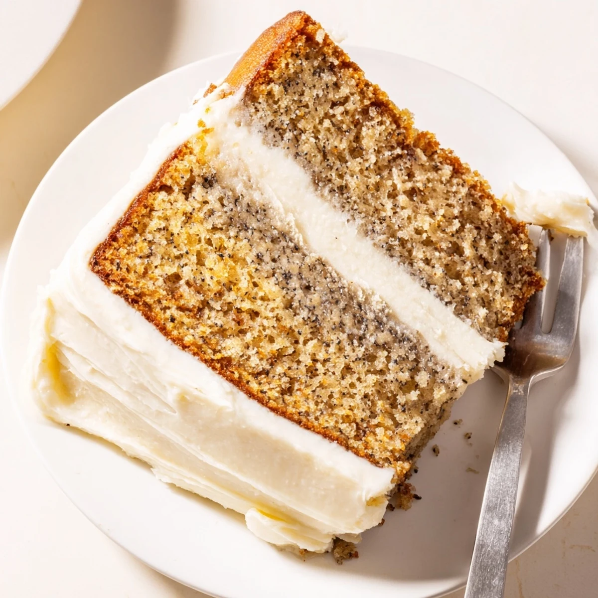A slice of brown butter banana cake with thick cream cheese frosting on a rustic plate