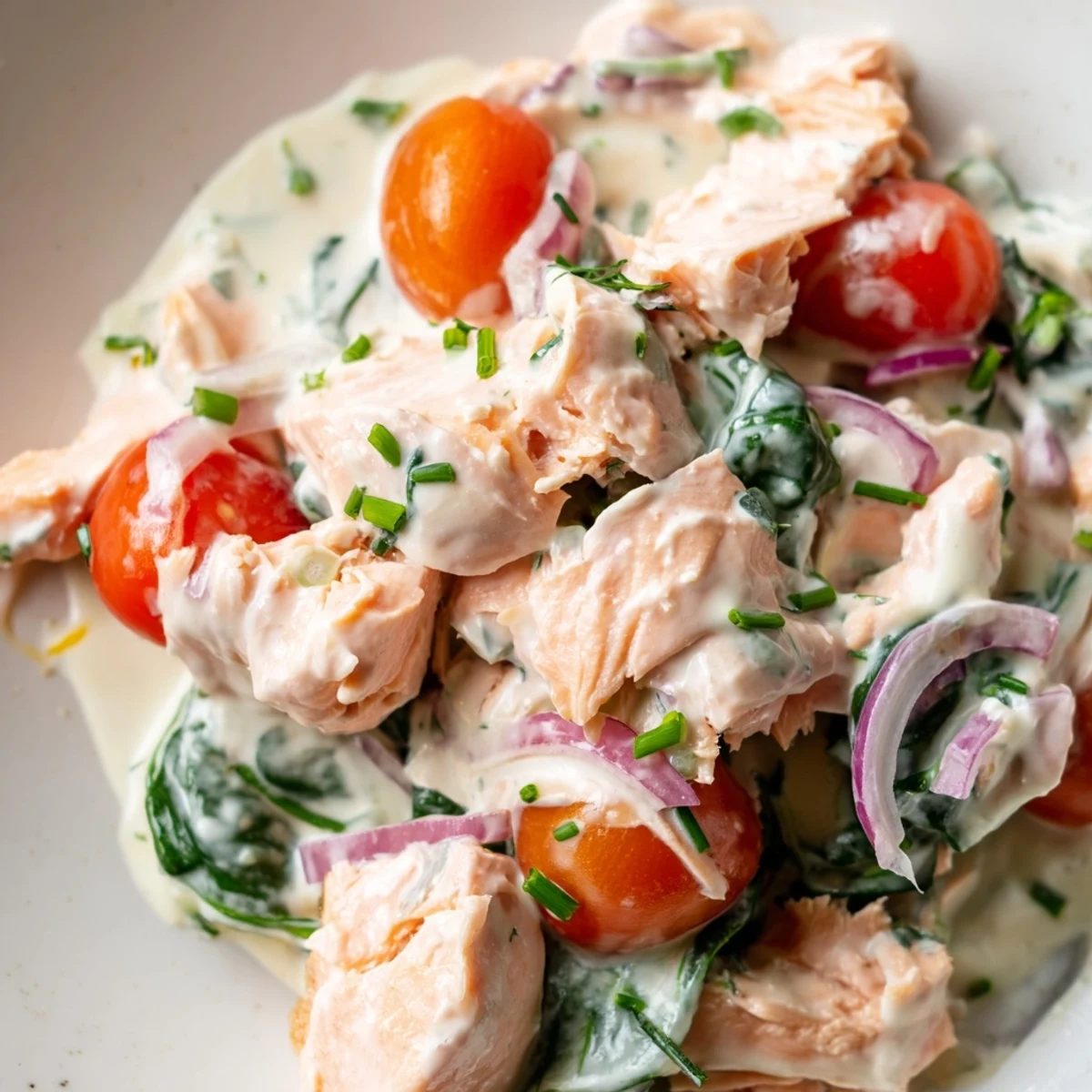 Creamy leftover salmon recipe in a golden skillet with wilted spinach and cherry tomatoes