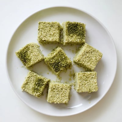 A close-up of a 5-Ingredient Matcha Halva slice reveals a creamy tahini and matcha swirl, served beside a warm cup of green tea.