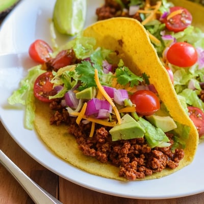 Warm tortillas holding savory Vegetarian Ground Beef Tacos with fresh lettuce, tomatoes, and a squeeze of zesty lime.