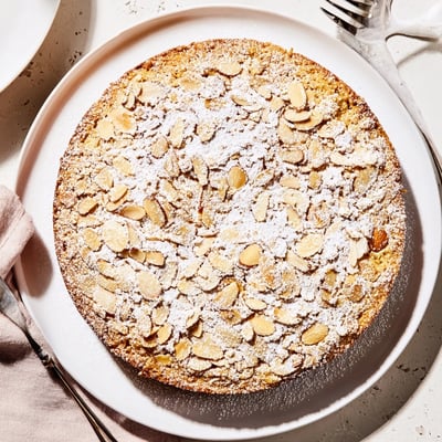 A moist almond cake slice on a plate with fresh berries and whipped cream.