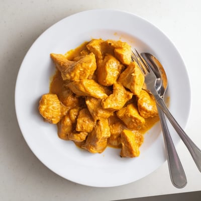 A warm skillet of 5 Ingredient Keto Butter Chicken garnished with fresh cilantro beside a fluffy cauliflower rice side.